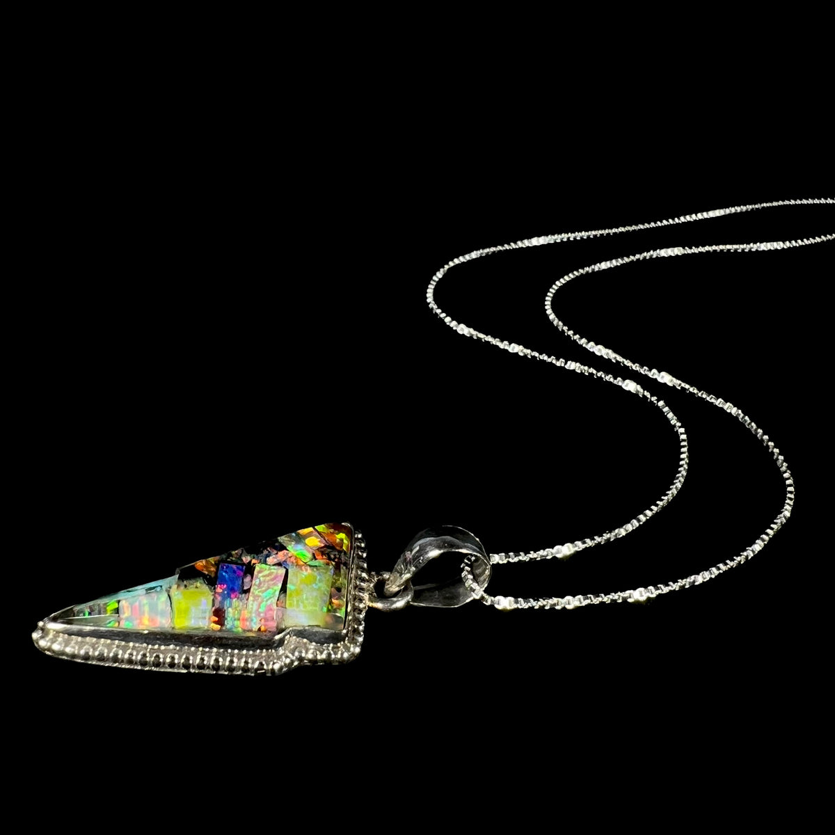 A Southwest-style sterling silver opal lightning bolt necklace shown laying on a black background, the pendant's box chain flowing into the distance.