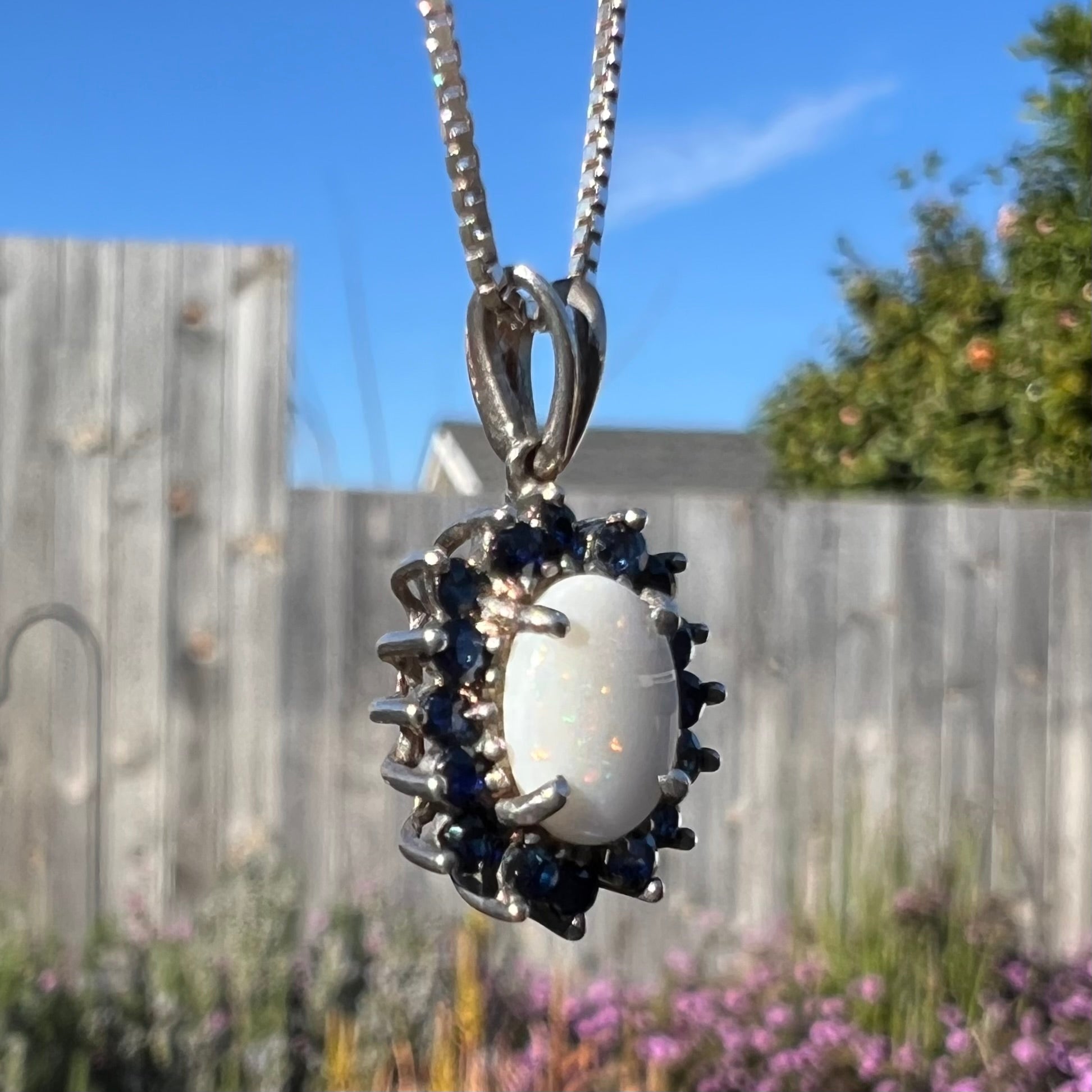 A macro close-up of a silver opal necklace outdoors, revealing faint orange pinfire flashes.