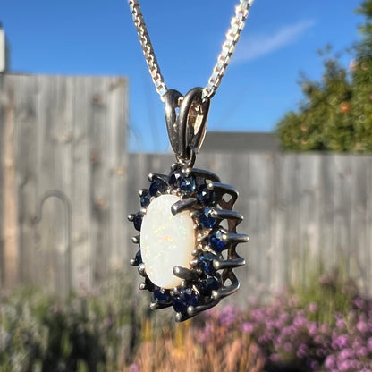 A side-angled macro view of a silver opal necklace in sunlight, showing a small orangish-red pinfire flash.