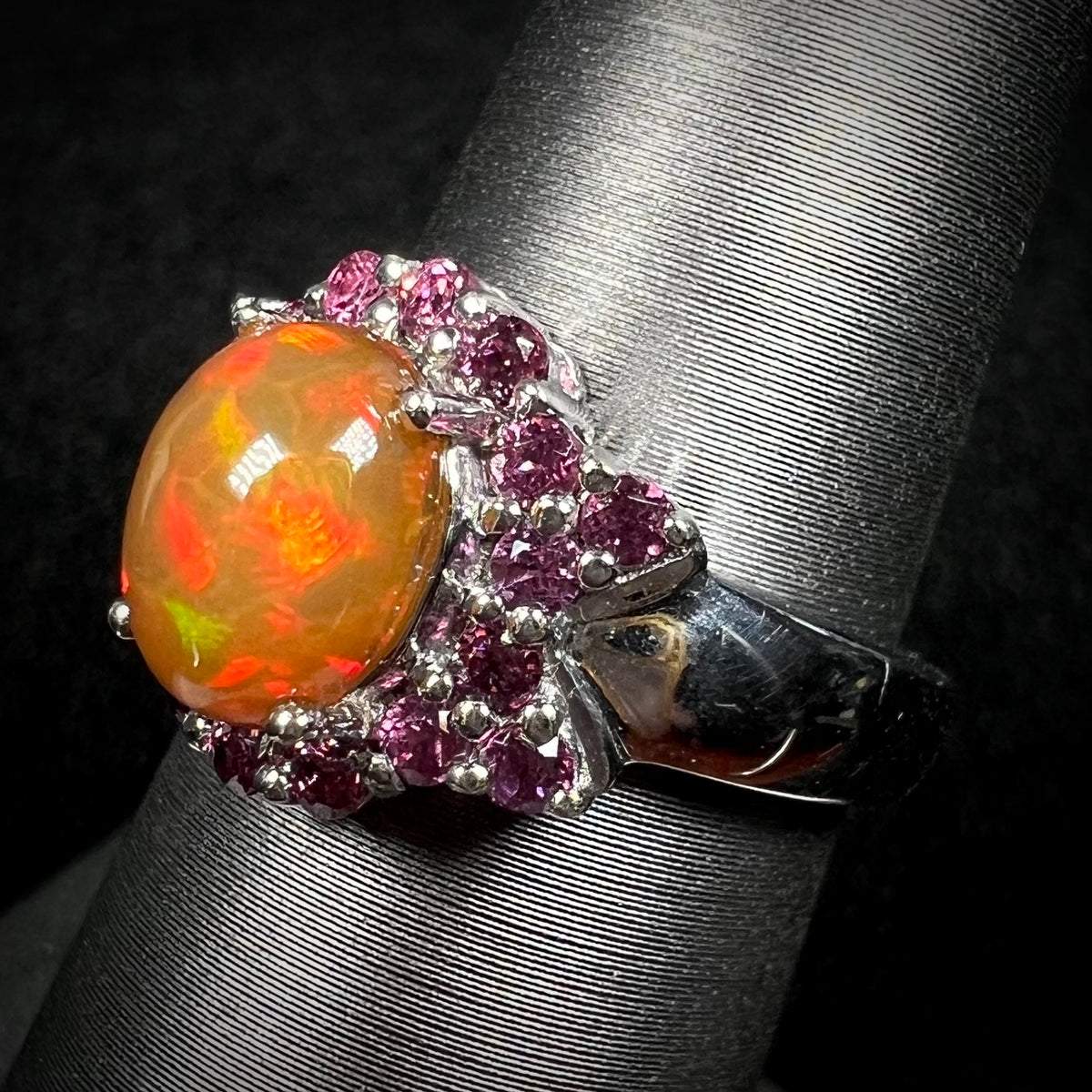 Close-up angled view of sterling silver Ethiopian fire opal and rhodolite garnet ring on display.  Opal has red flashes of color
