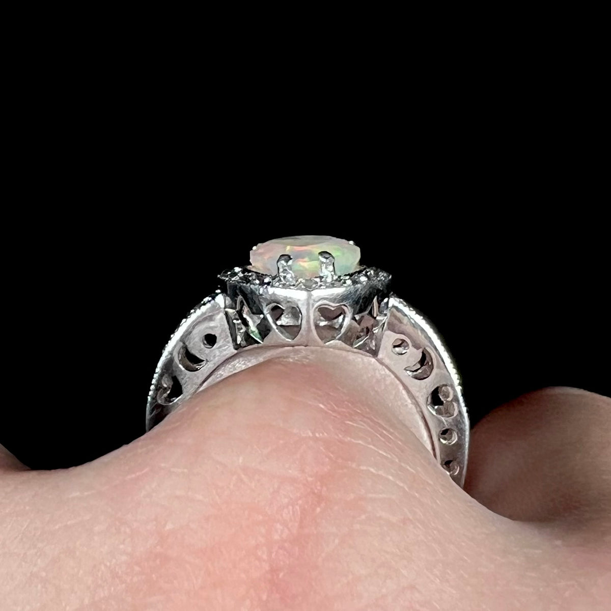 Side profile gallery view of sterling silver opal ring worn on finger, showing cutout heart, star, and crescent moon shapes along ring's gallery and shank