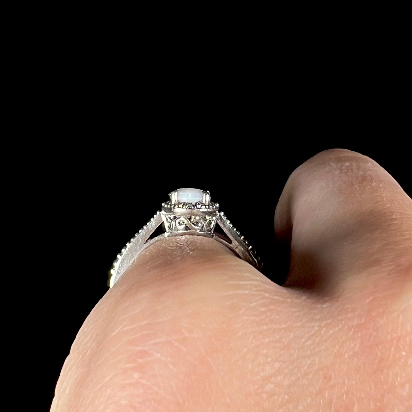 Side gallery profile view of a silver opal ring worn on a hand, showing the filigree design on its basket.