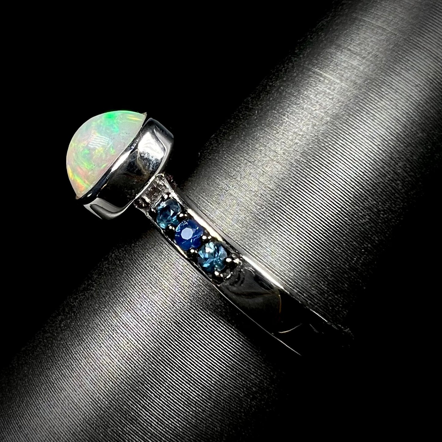 Side view of silver opal ring against black background.  Ring's shank and topaz accents in focus.