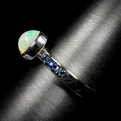 Side view of silver opal ring against black background.  Ring's shank and topaz accents in focus.