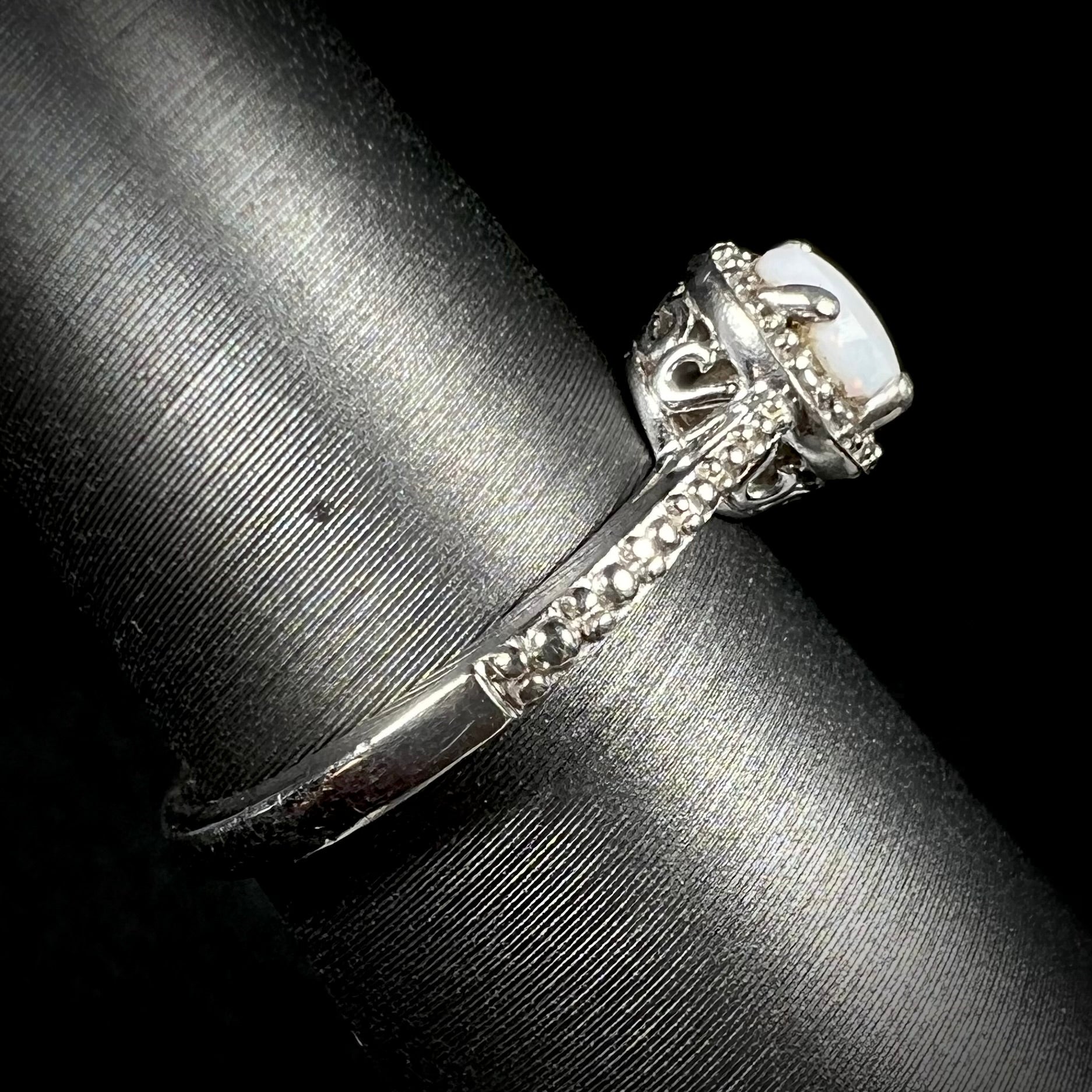 The side shank and filigree design of a sterling silver white opal and diamond ring with a halo design.