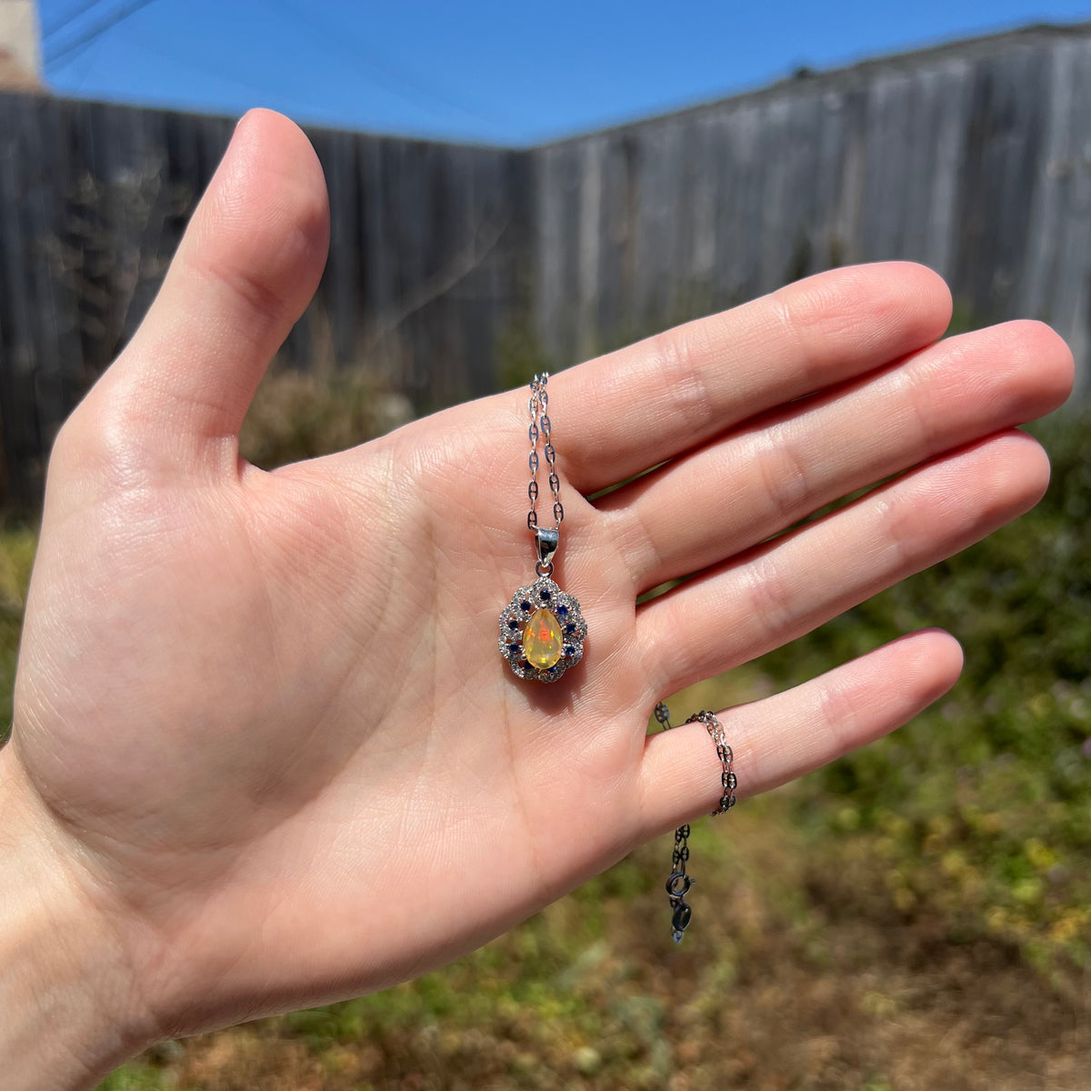 Hand holding women's sterling silver blue sapphire and Ethiopian opal necklace in sunlight