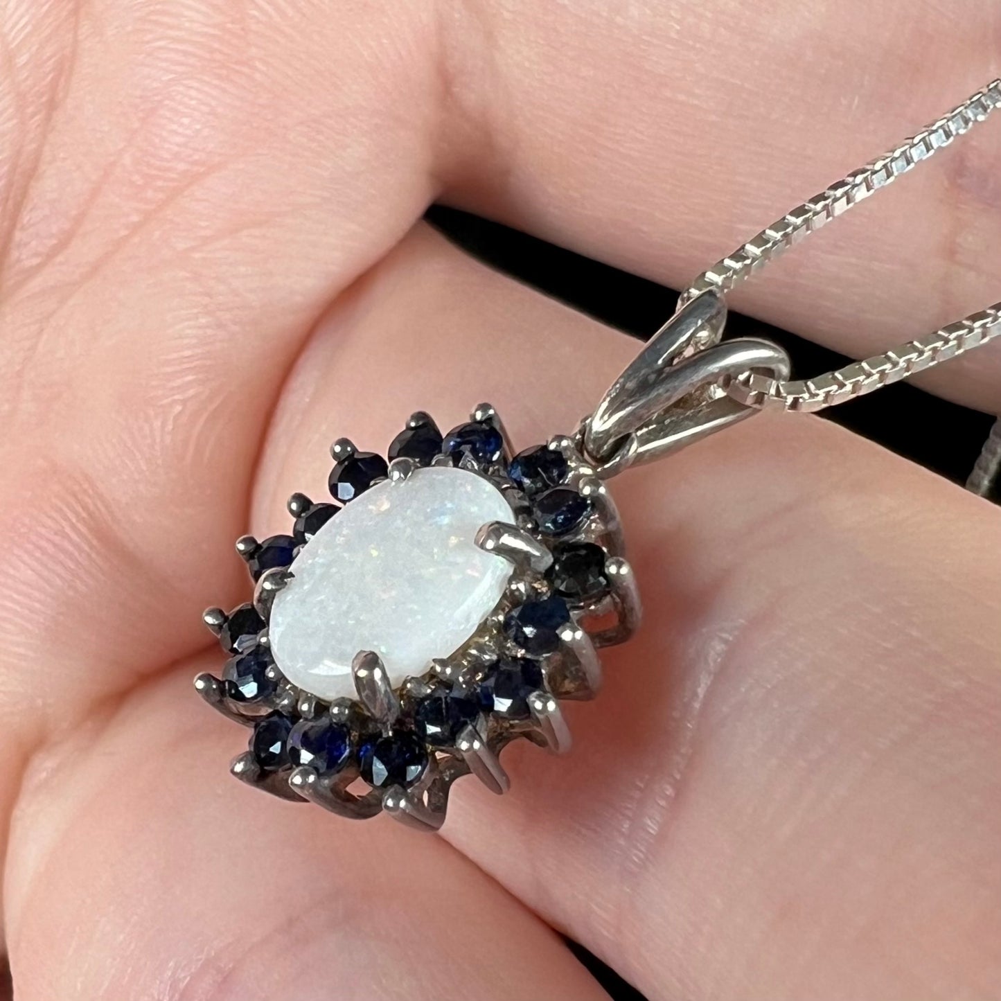 A side-angle view of a silver opal and sapphire necklace, showcasing its delicate prong setting.