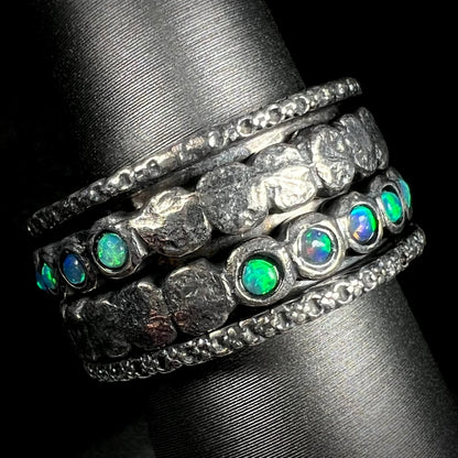 A sterling silver opal spinner ring for men with a hammered texture, shown at an angle against a black backdrop.