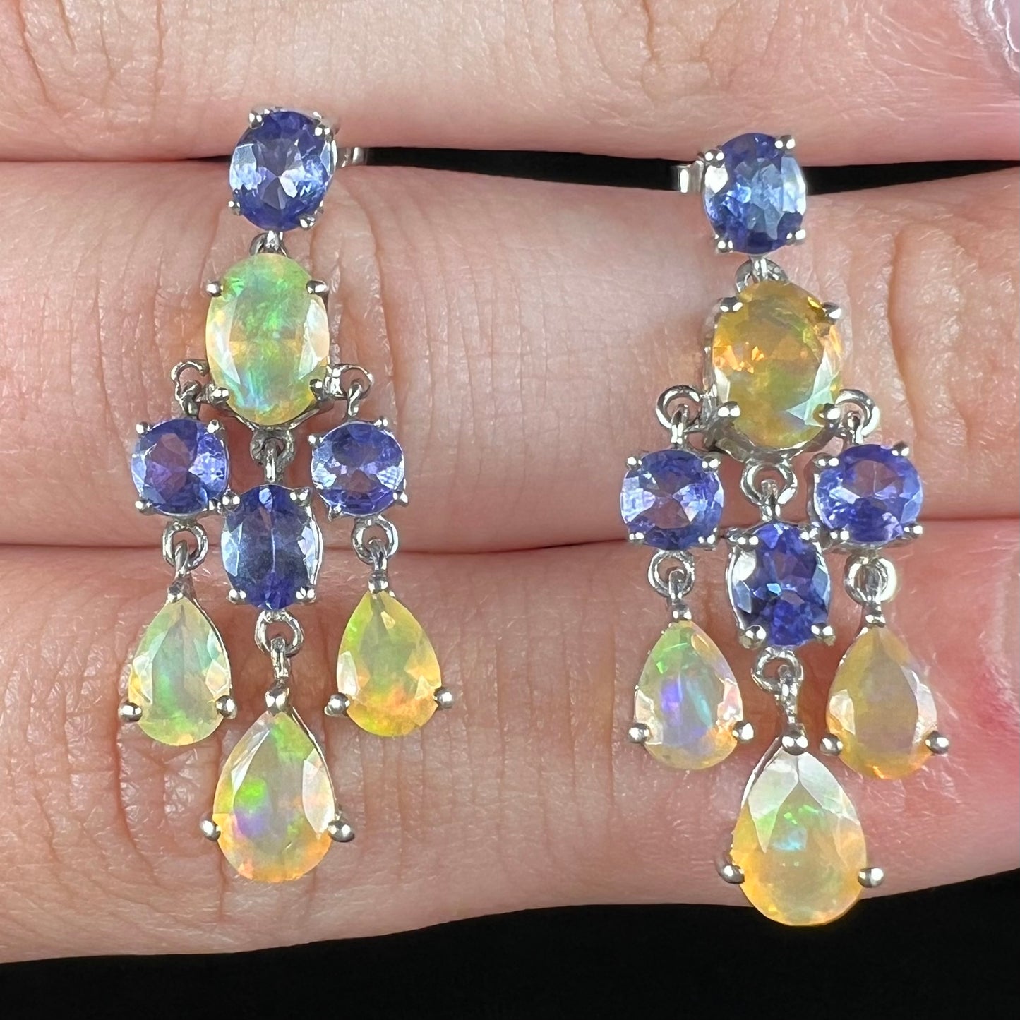 A pair of dangling sterling silver Ethiopian opal and tanzanite chandelier earrings shown close-up.