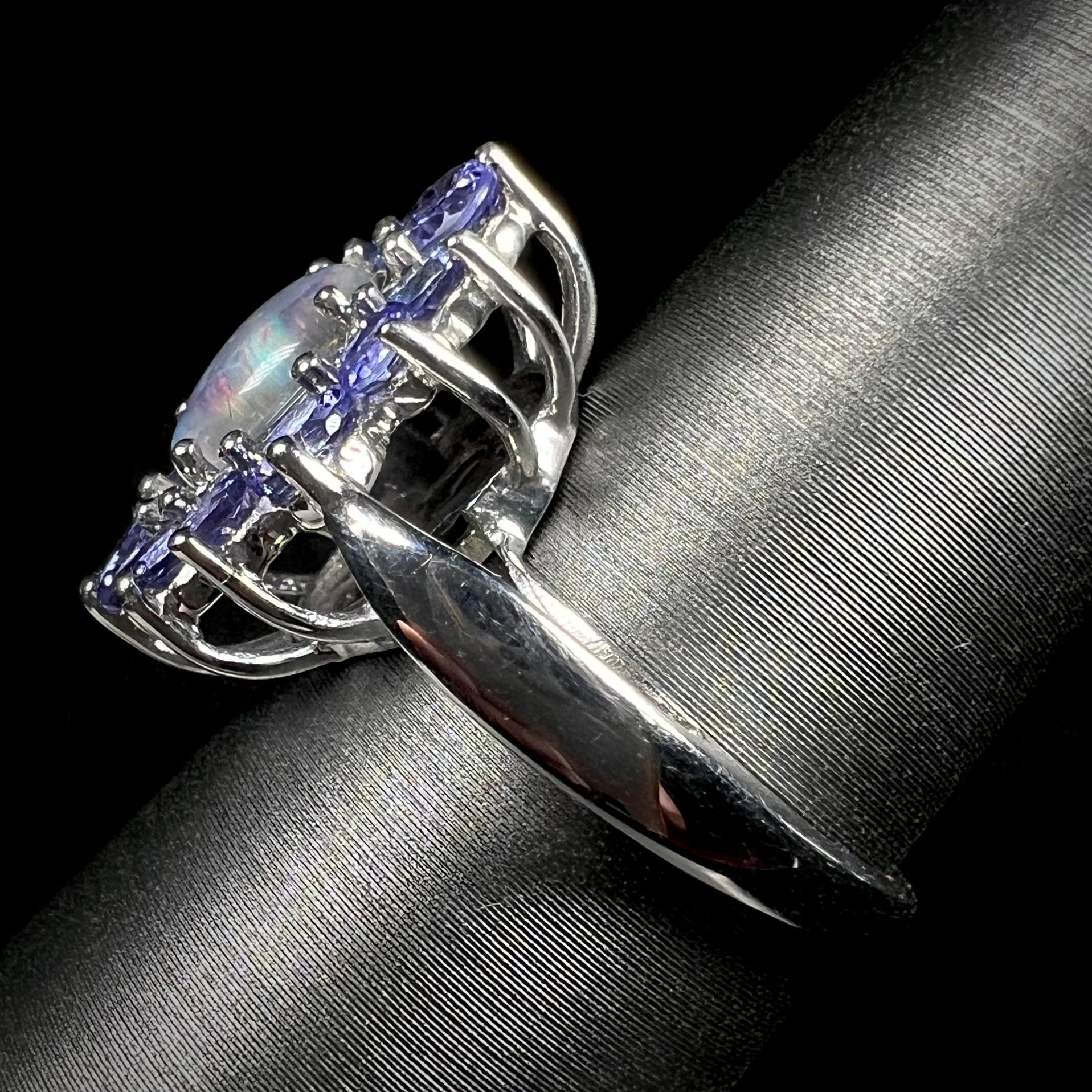 The side angle view of a silver ring mounted with a black opal triplet in a halo of tanzanite stones.