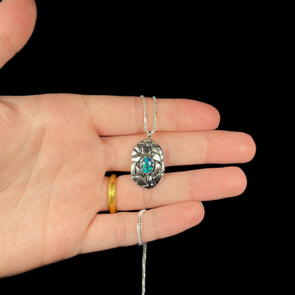 A unisex sterling silver pinecone-inspired opal triplet necklace shown in a hand against a black background.