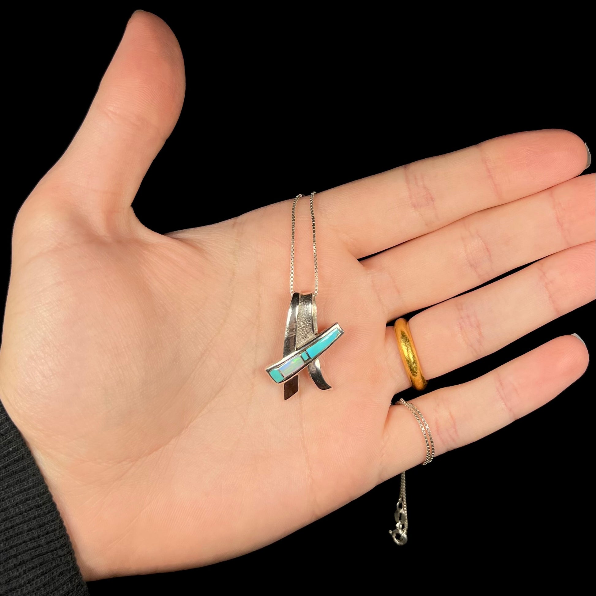 A folded design sterling silver turquoise and lab-created opal inlay necklace shown in a hand.