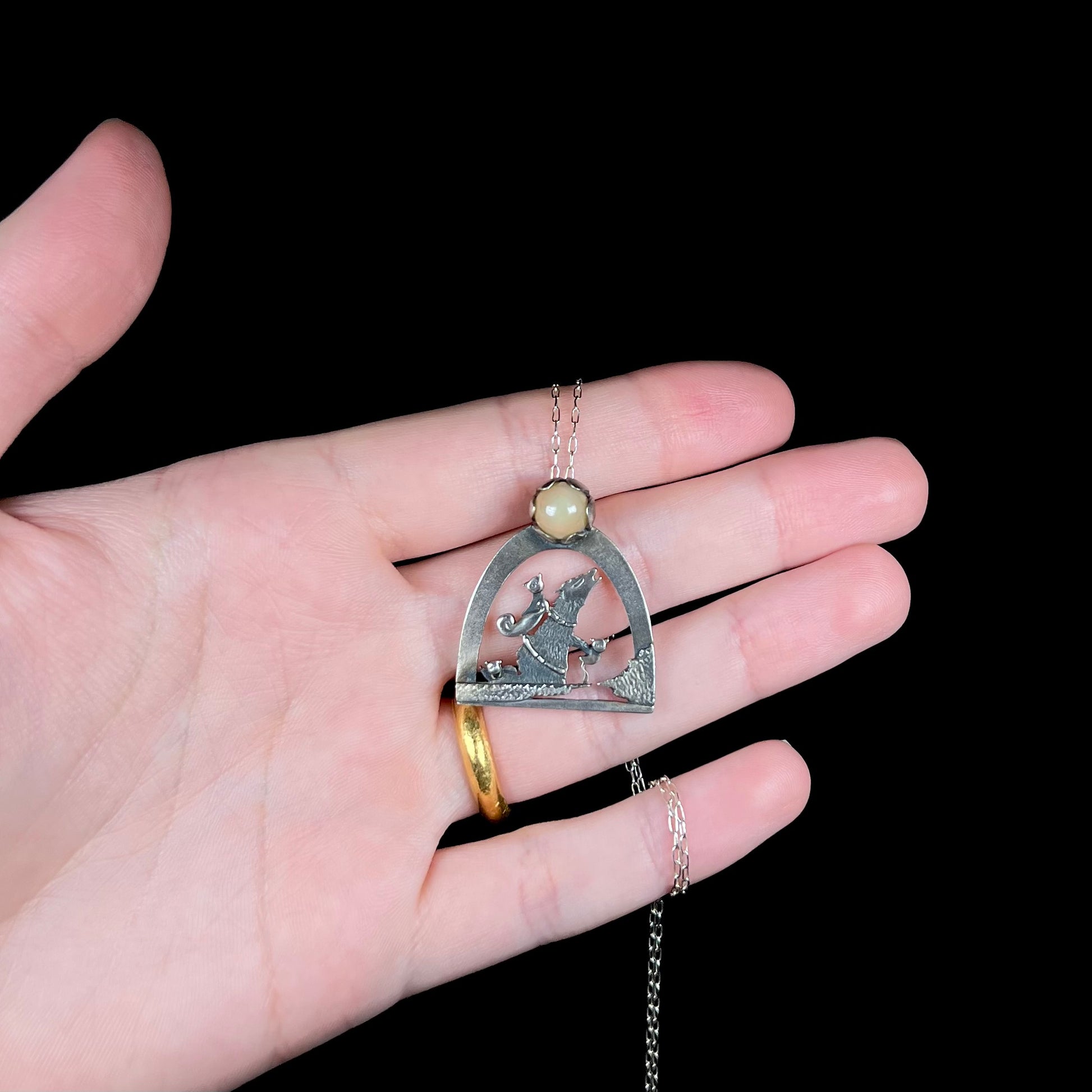 A sterling silver Ethiopian opal wolf and cat design necklace, held in a hand against a black background.
