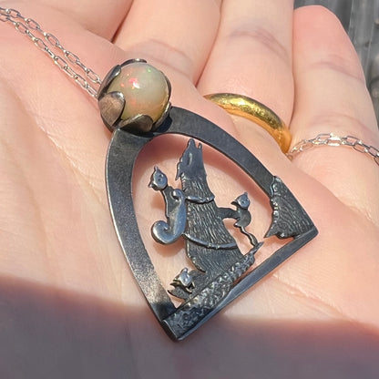 Angled close-up of a sterling silver Ethiopian opal wolf and cat design necklace in sunlight, shown in a hand.