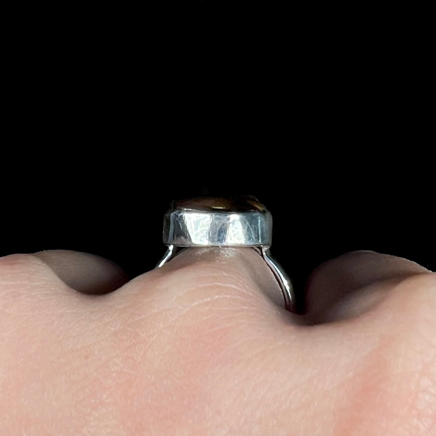 Side profile gallery view of a silver ring worn on a hand.