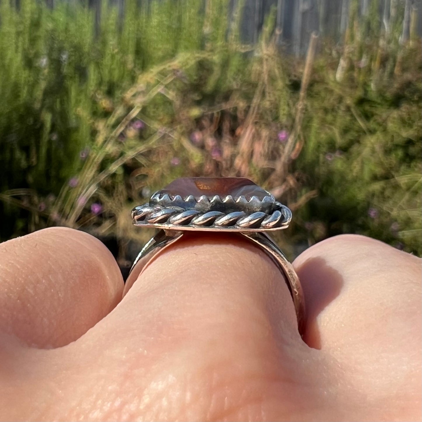 Side gallery view of a silver fire agate ring with a rope design, worn on a finger in sunlight.