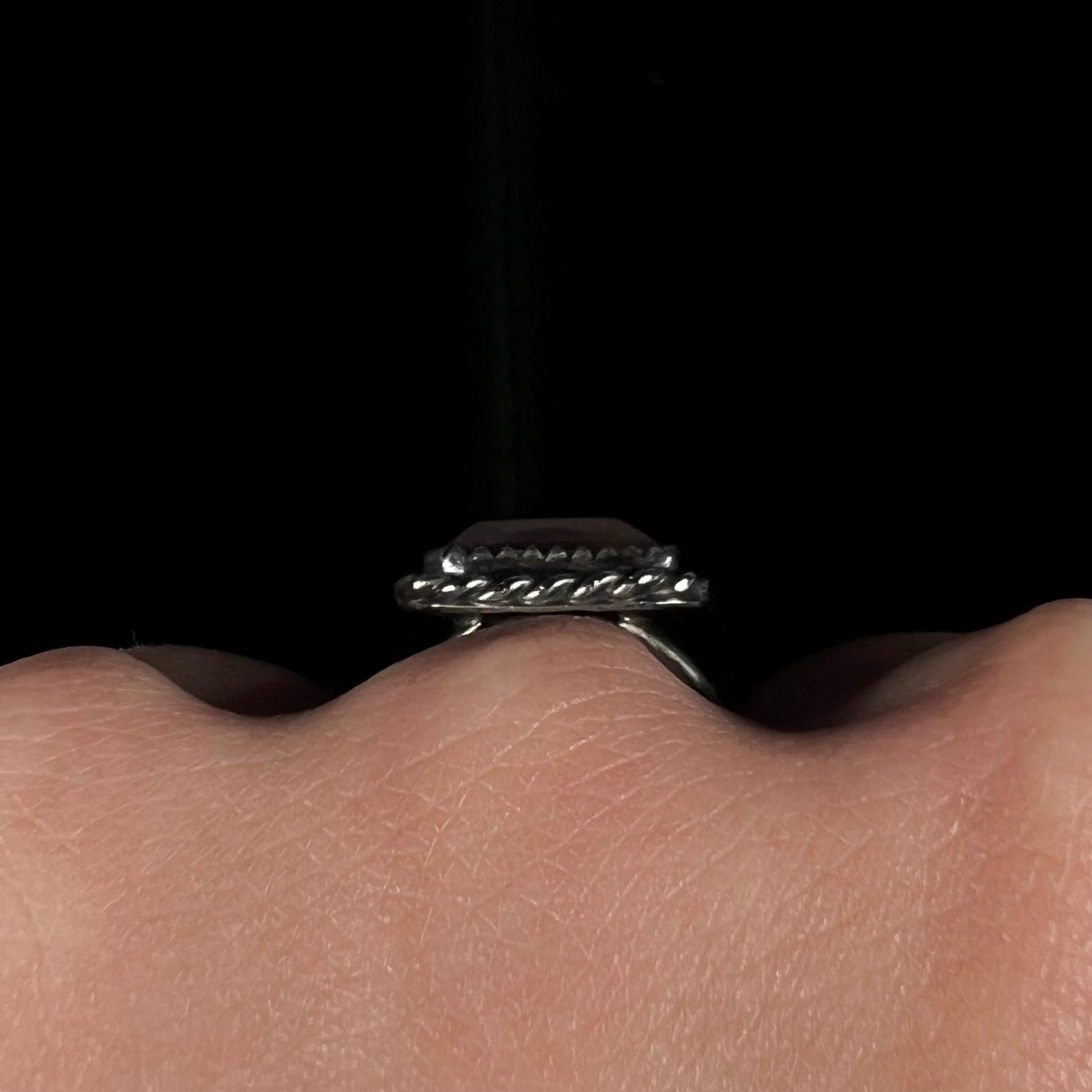 Side gallery view of the silver rope bezel on a fire agate ring, worn on a hand against a dark background.