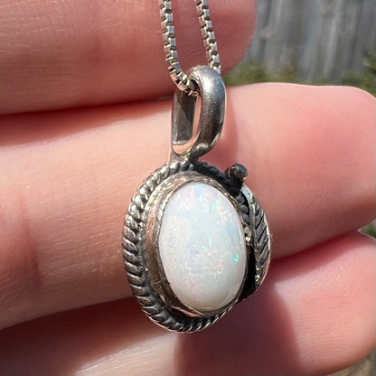 Angled close-up of silver rope bezel pendant set with white Australian opal, held under natural sunlight