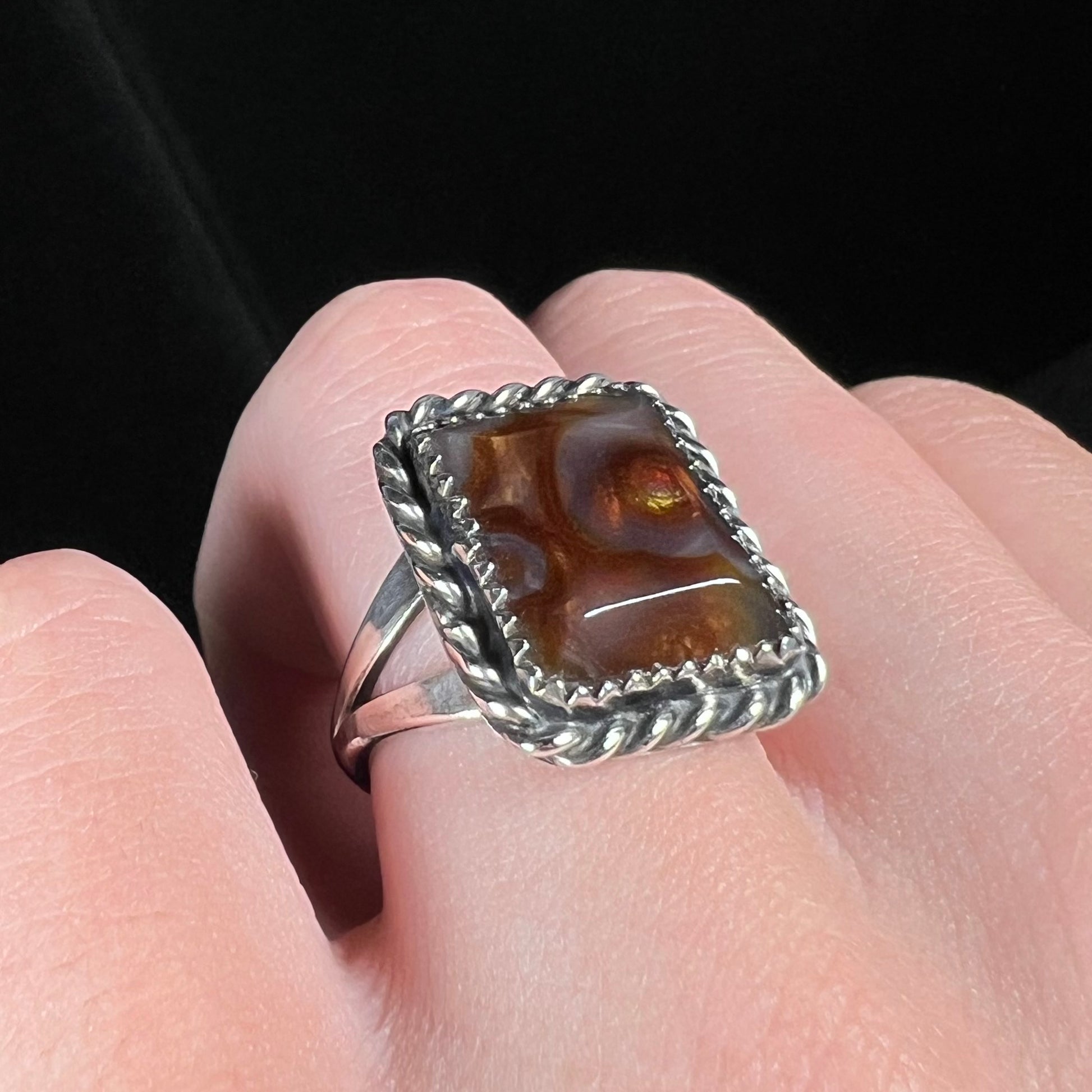 Angled view of a sterling silver rope design fire agate ring with a split shank, worn on a finger.