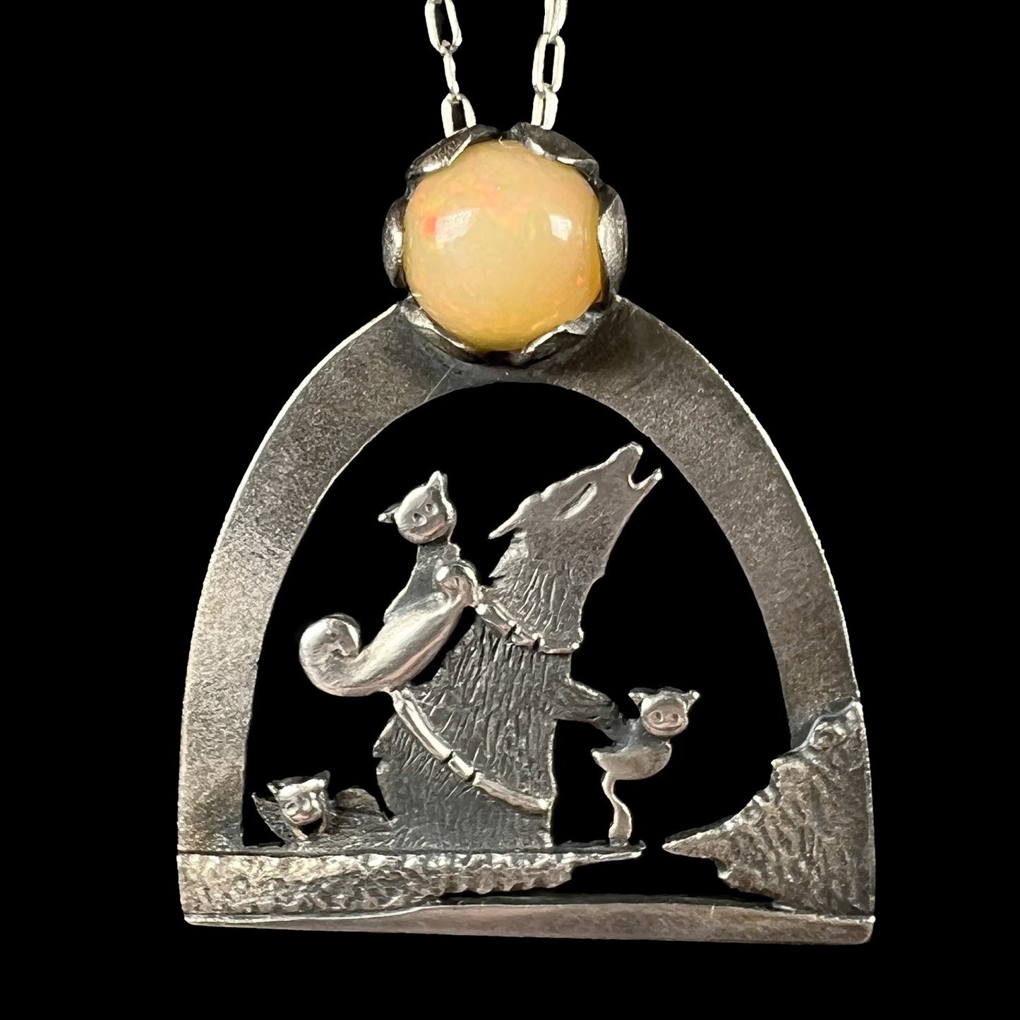 A sterling silver necklace with the design of three cats riding a wolf as the wolf howls at the moon.