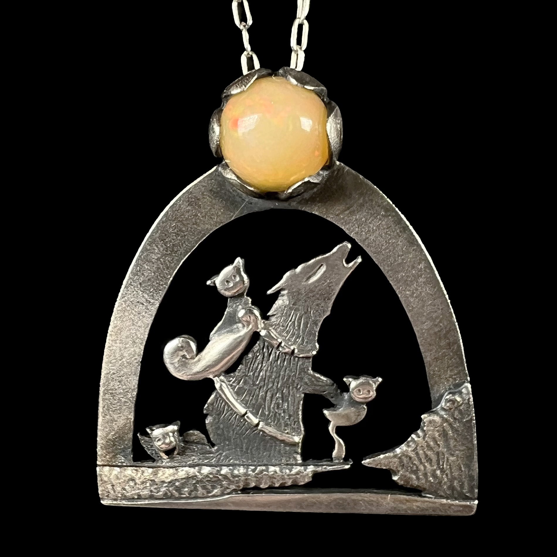 A sterling silver necklace with the design of three cats riding a wolf as the wolf howls at the moon.
