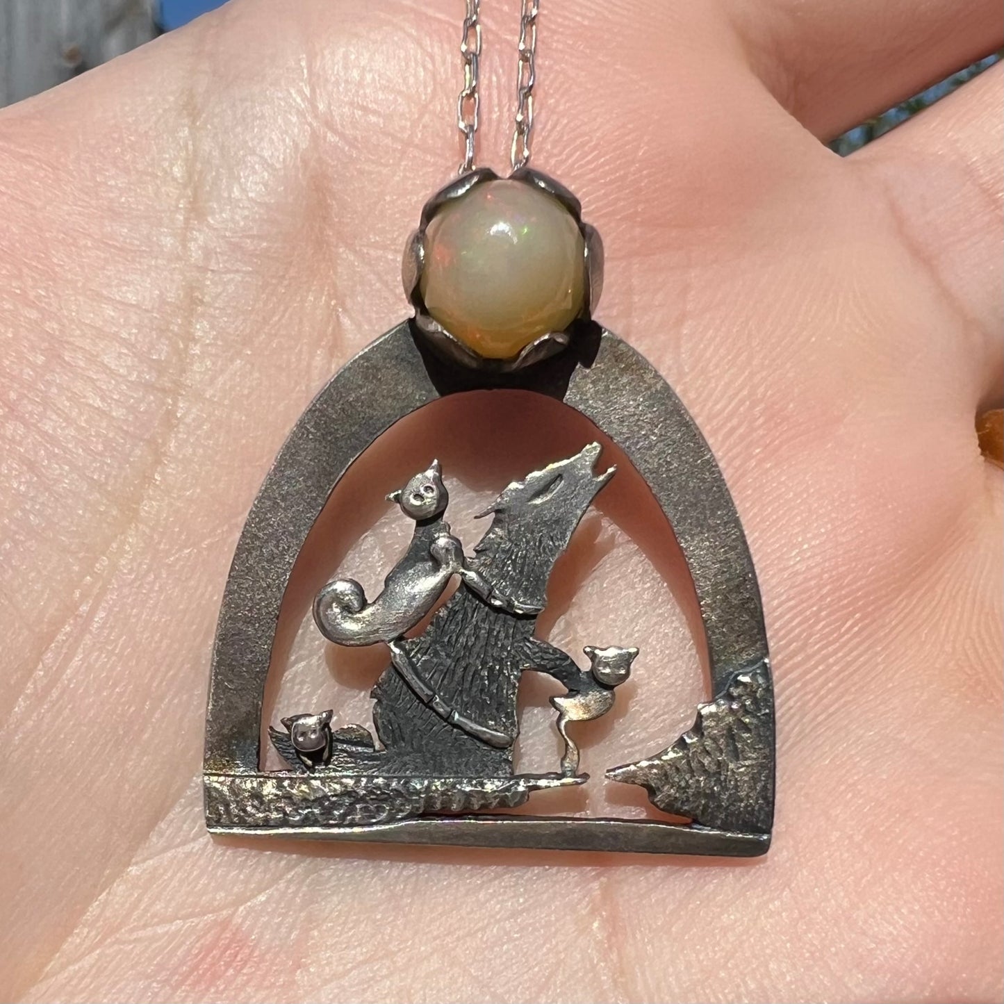Close-up of a sterling silver Ethiopian opal wolf and cat design necklace in sunlight, held in a hand.