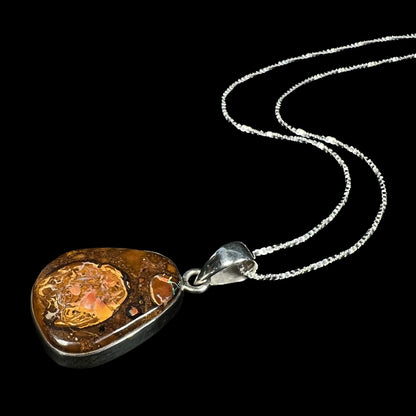 A Yowah nut boulder opal necklace in sterling silver, shown from an angle laying against a black backdrop.