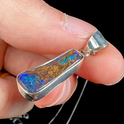 A sterling silver necklace bezel set with a natural Australian boulder opal stone.  The stone shines colors of blue, green, and purple.