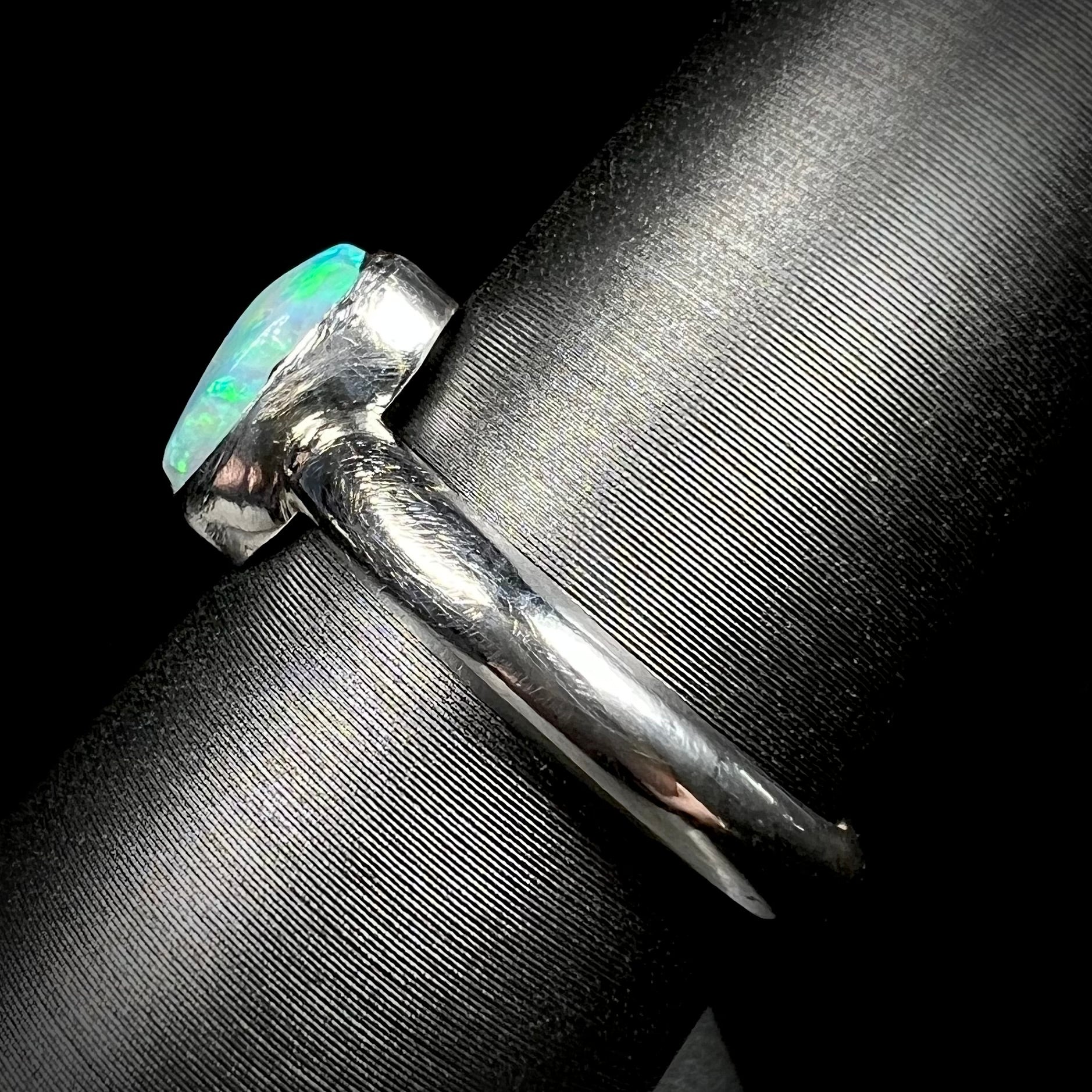 Side shank view of a simple handmade silver opal solitaire ring on a ring display.