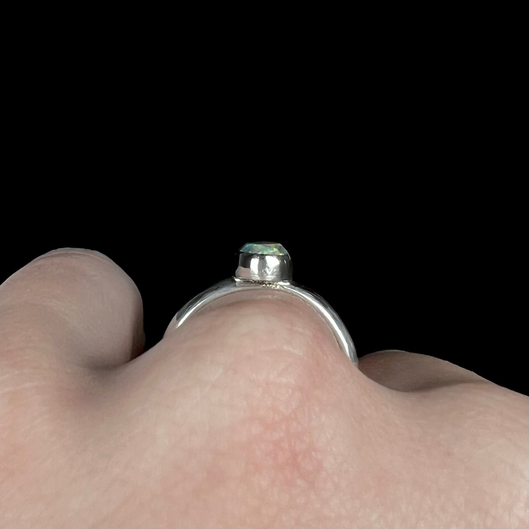 Side profile gallery view of a simple, handmade sterling silver opal ring worn on a hand.