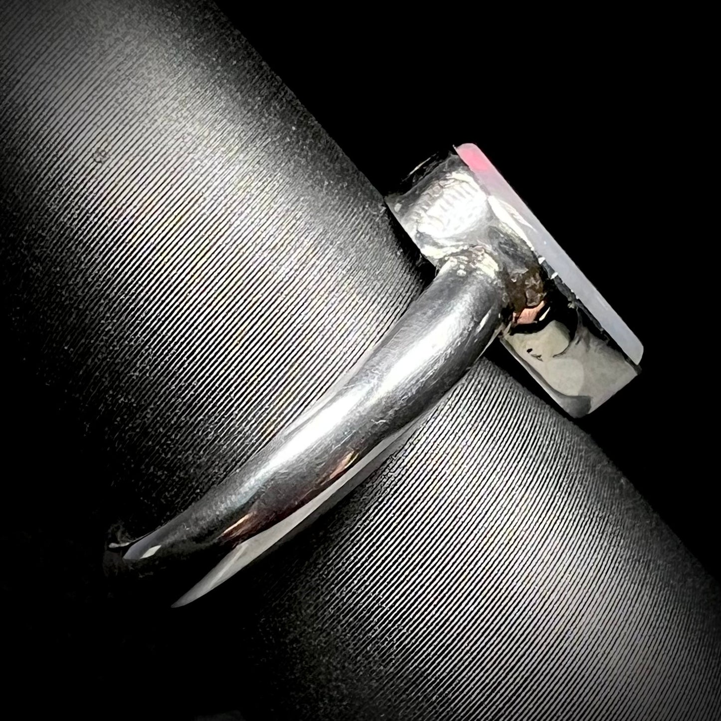 Side profile view of a simple sterling silver opal ring on a ring display, its polished shank in focus.