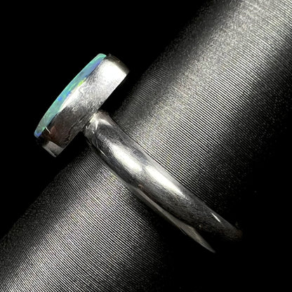 Side view of a simple sterling silver solitaire ring set with an opal, shown on a ring display.  The ring's shank and bezel setting are in focus.