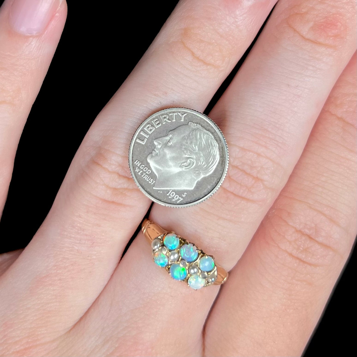 Antique six-stone Australian opal and pearl ring worn on middle finger of hand next to US dime coin for scale
