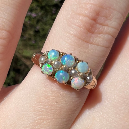 Close-up of six-stone Victorian era opal ring with pearl accents in 9k gold, worn on finger in sunlight