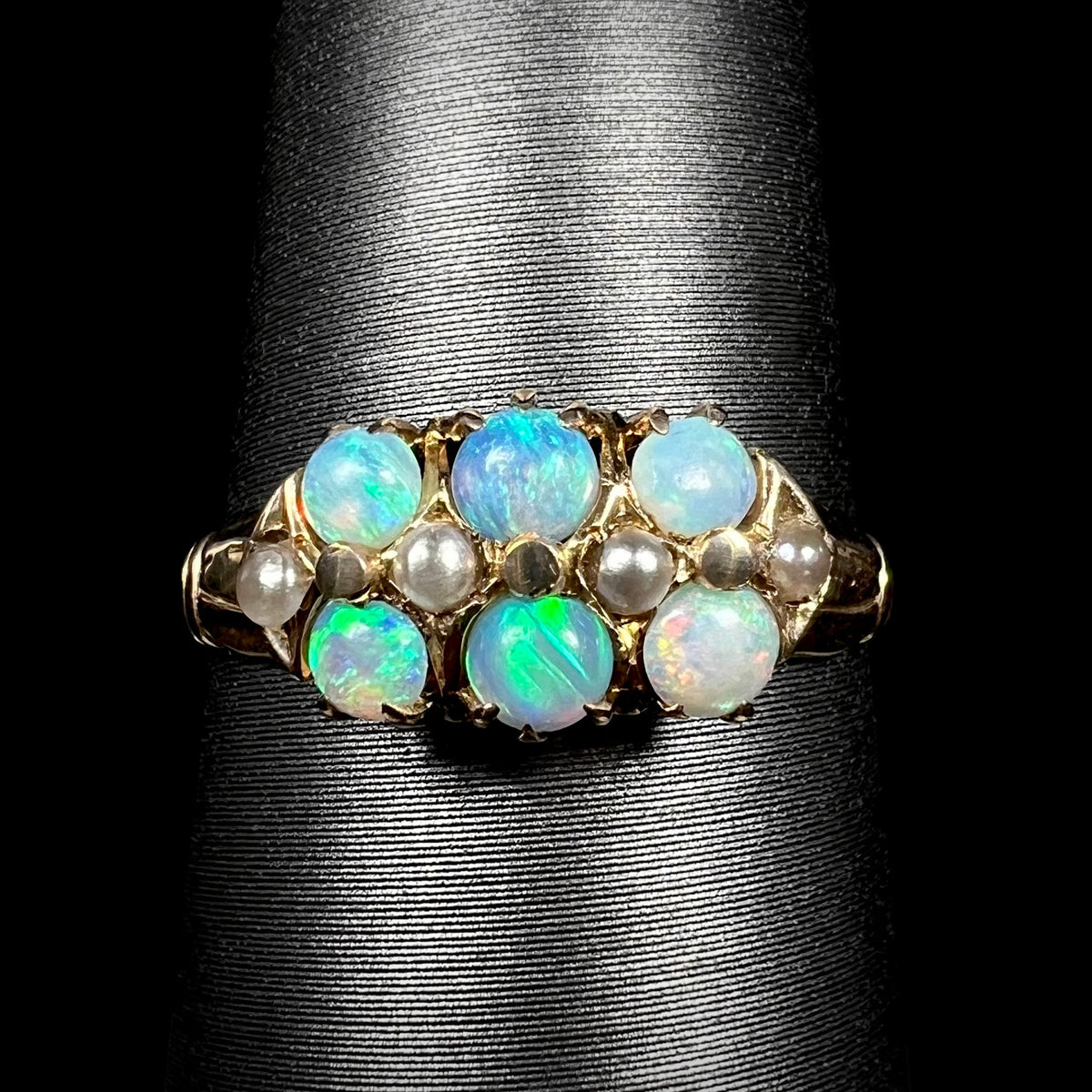 Close-up of 9k gold Victorian six-stone ring set with round Australian opals and pearl accents, shown on ring display