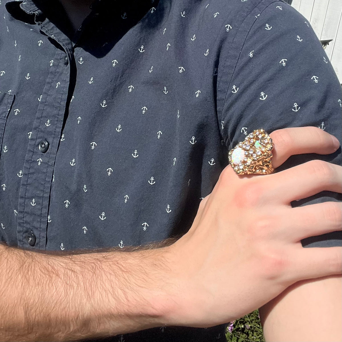Close-up of person resting hand on opposing shoulder in sunlight wearing a large, size 11 lab-created opal and CZ costume ring.