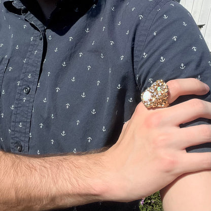 Close-up of person resting hand on opposing shoulder in sunlight wearing a large, size 11 lab-created opal and CZ costume ring.