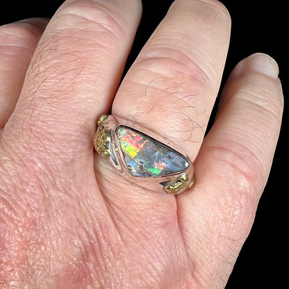 Close-up view of a size 12 sterling silver boulder opal ring worn on a man's finger against a black backdrop.  The opal has red, orange, and flashes in studio light.
