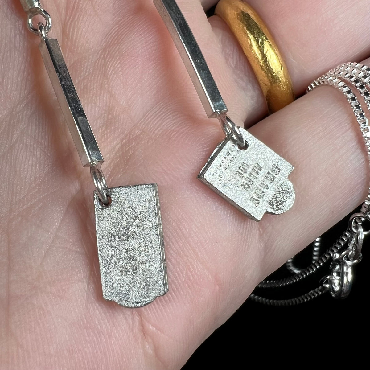 Base metal tombstone-shaped feet shown close-up, attached to sterling silver "leg bones" of skeleton pendant, held in hand