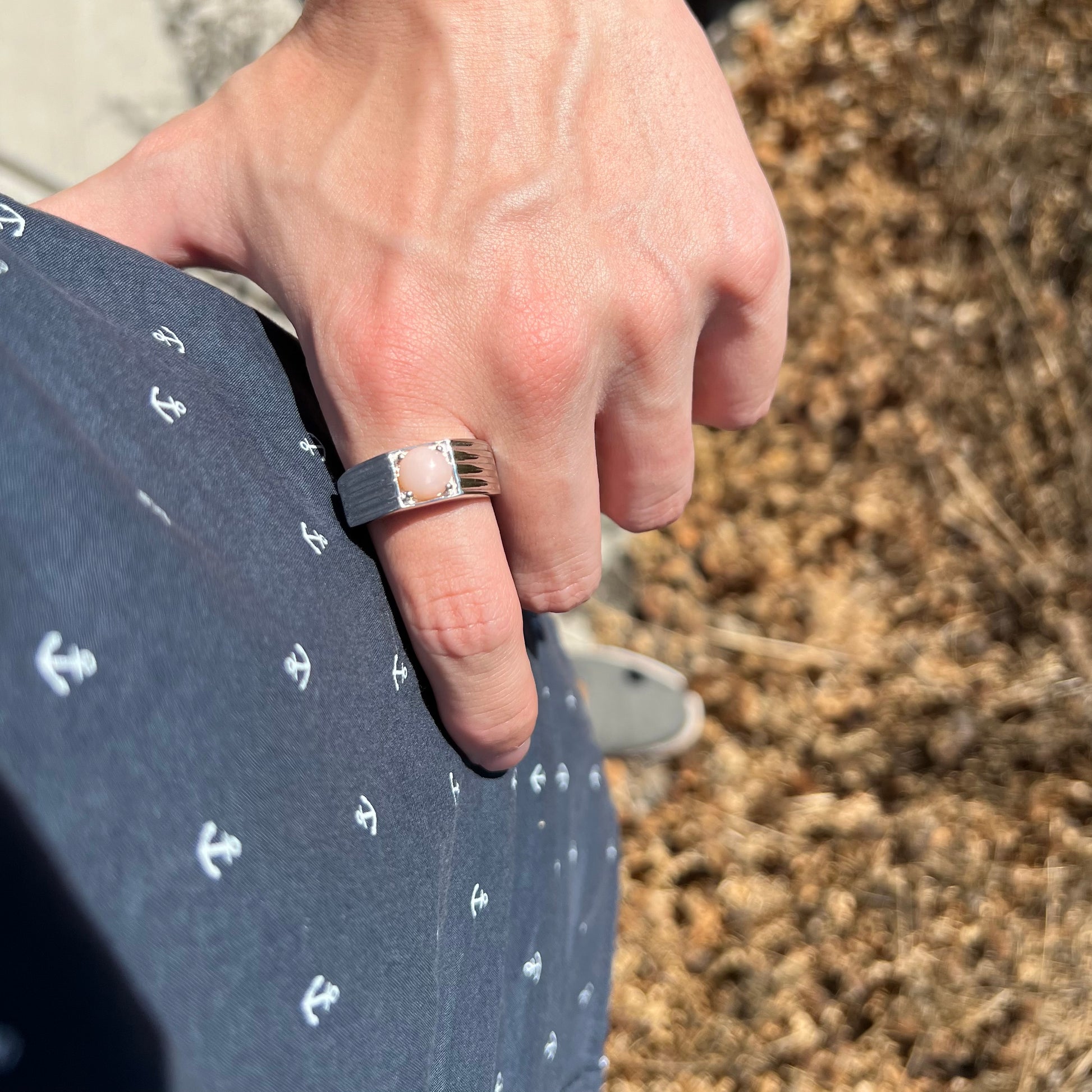 Hand resting on man's hip while wearing sleek sterling silver pink Peruvian opal men's ring in sunlight