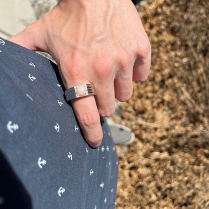 Hand resting on man's hip while wearing sleek sterling silver pink Peruvian opal men's ring in sunlight