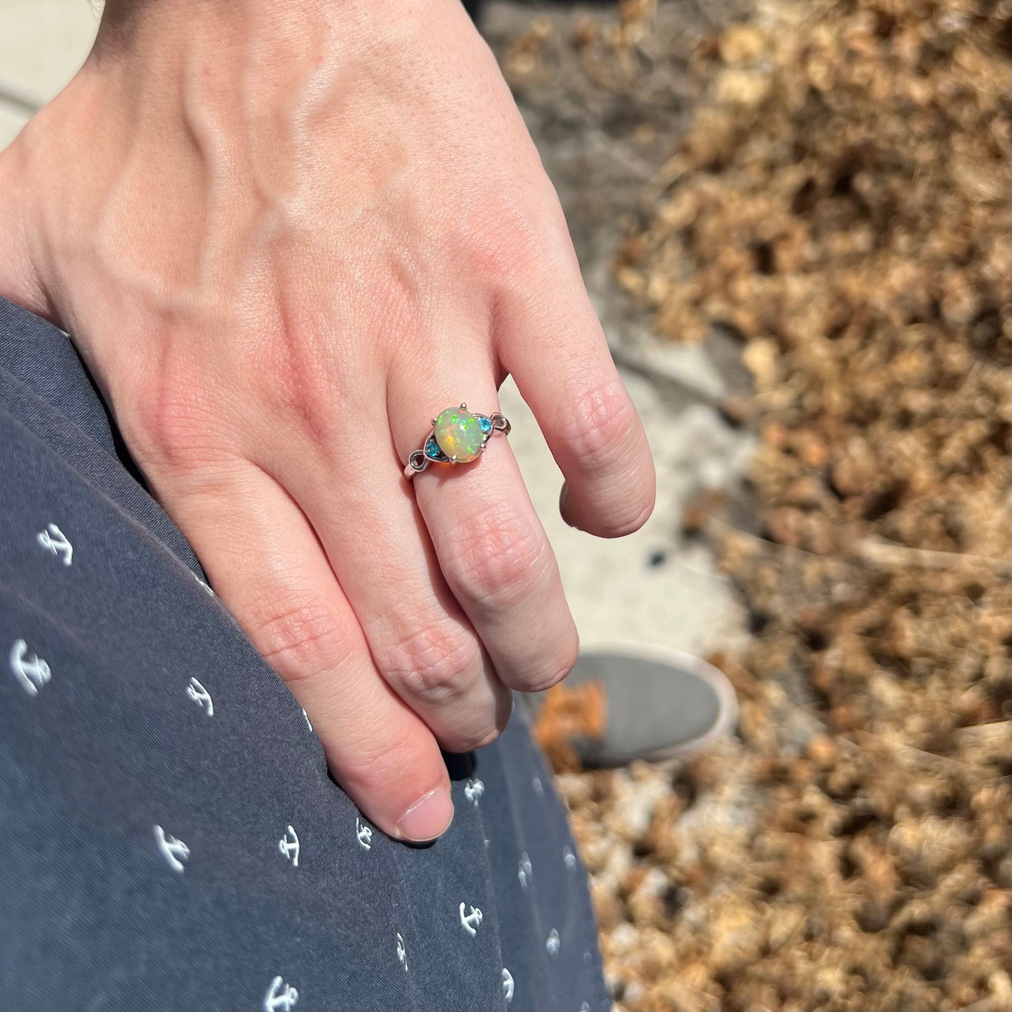 Hand resting on hip in sunlight while wearing small Ethiopian opal and blue apatite silver ring