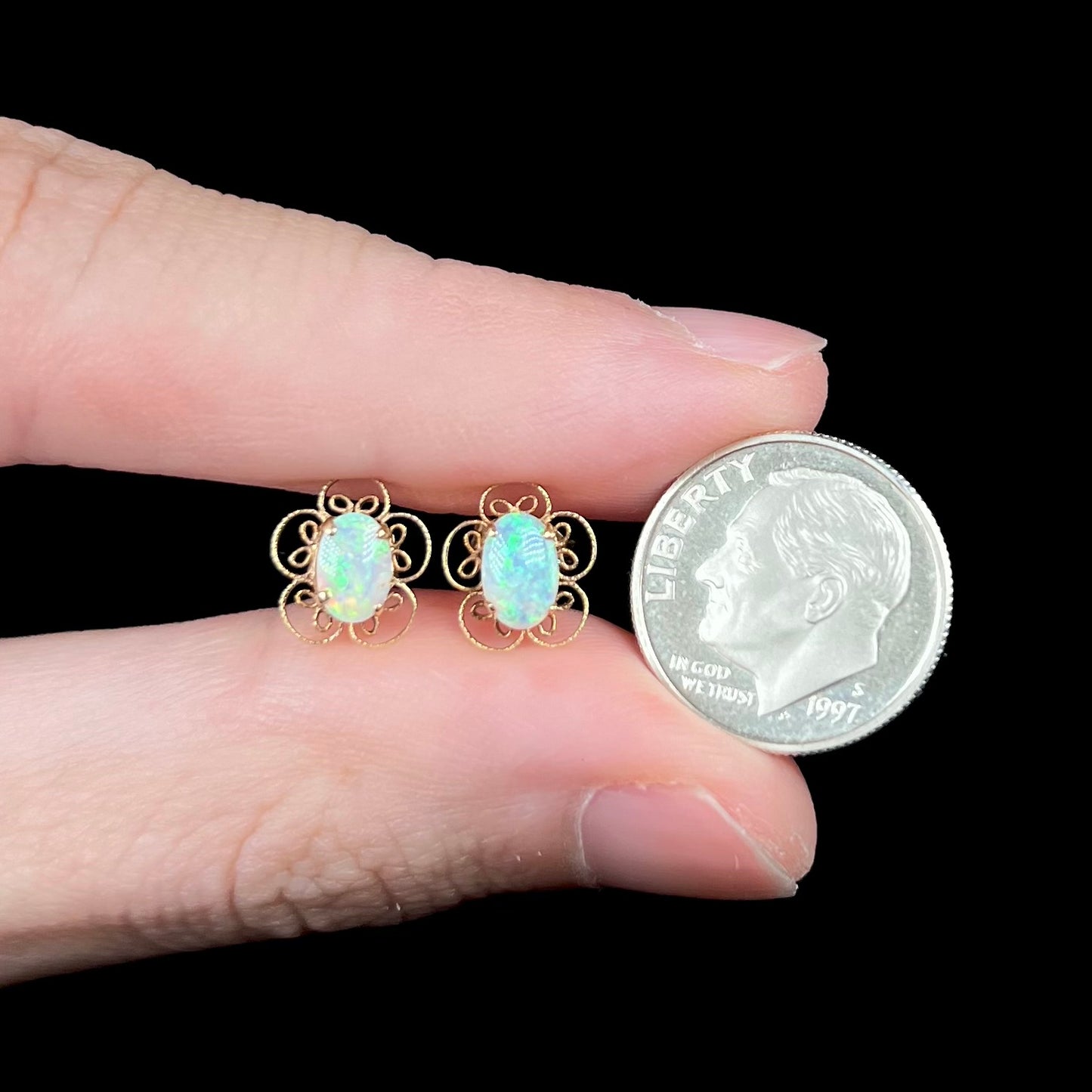 Small 14k gold opal stud earrings with flower design held between fingers with US dime coin