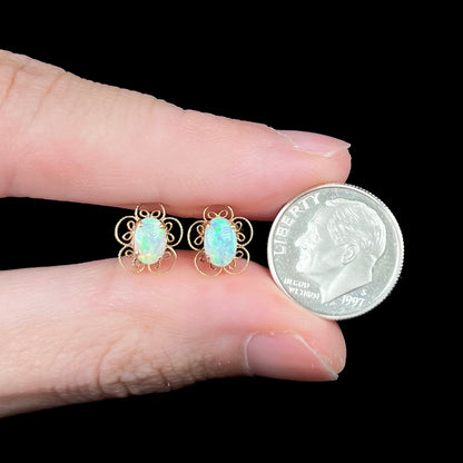 Small 14k gold opal stud earrings with flower design held between fingers with US dime coin