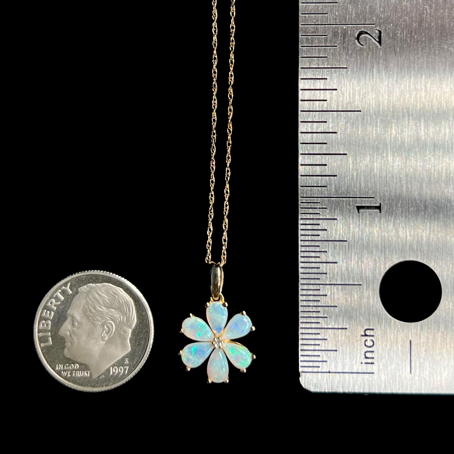 Small, delicate opal and diamond cluster flower pendant shown next to US dime coin and ruler for scale