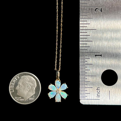 Small, delicate opal and diamond cluster flower pendant shown next to US dime coin and ruler for scale
