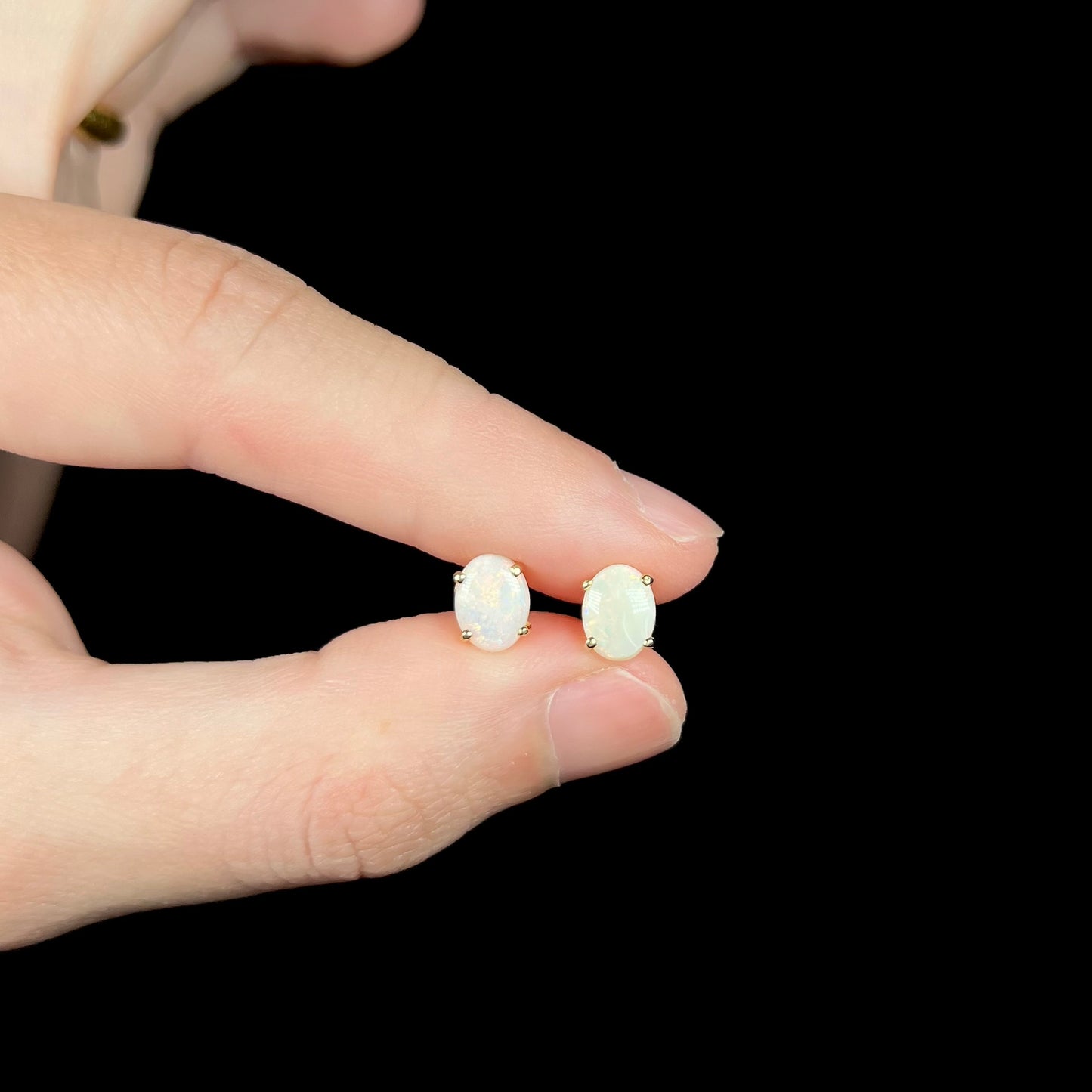 Small opal stud earrings held between fingers