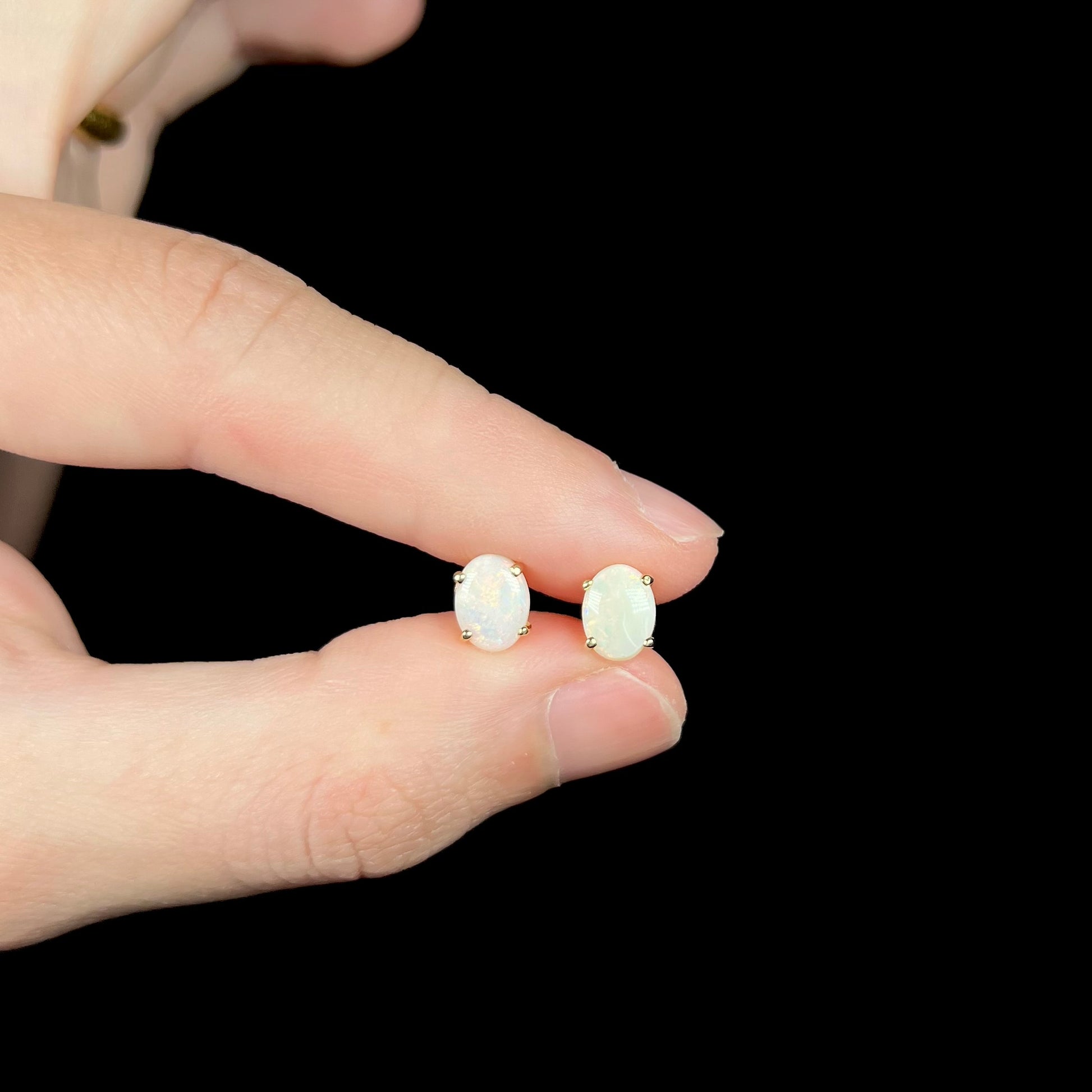 Small opal stud earrings held between fingers