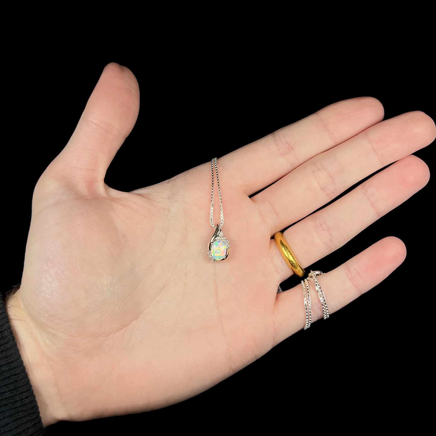 A small sterling silver and 10k gold two-tone opal and diamond necklace held in a hand.
