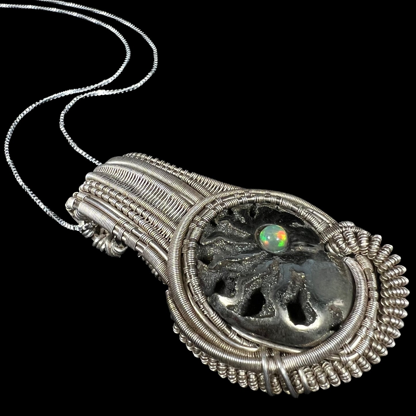 Angled close-up of men's silver wire wrapped pendant set with pyritized ammonite snail fossil and colorful Ethiopian opal accent.